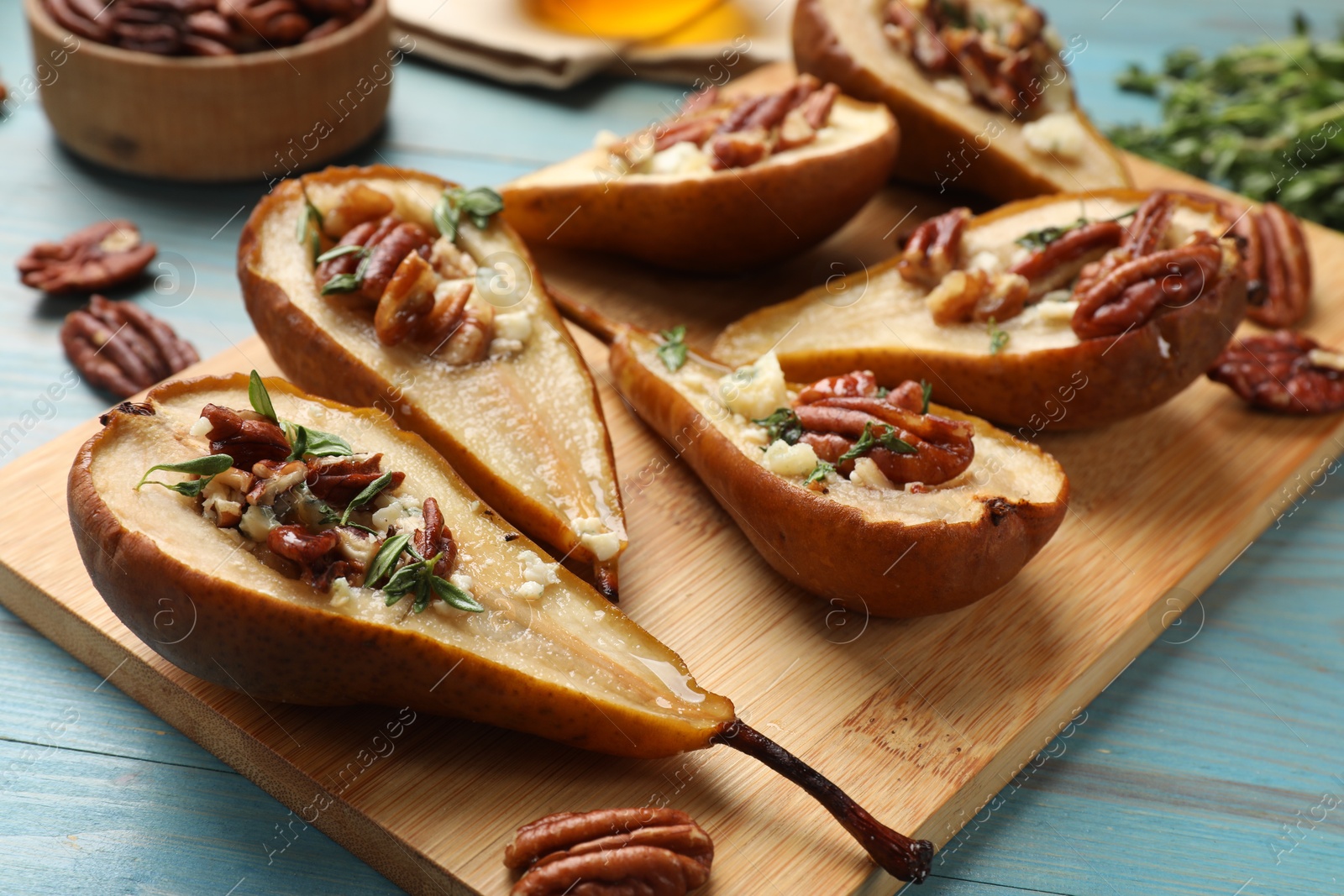 Photo of Delicious baked pears with nuts, blue cheese, thyme and honey on light blue wooden table, closeup