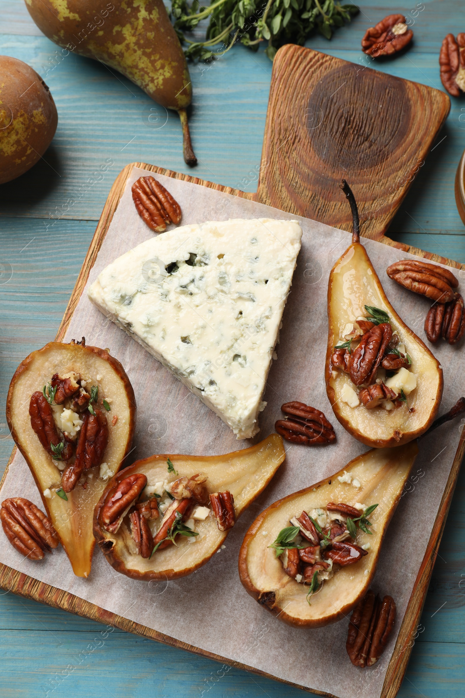 Photo of Delicious baked pears with nuts, blue cheese, thyme and honey on light blue wooden table, flat lay