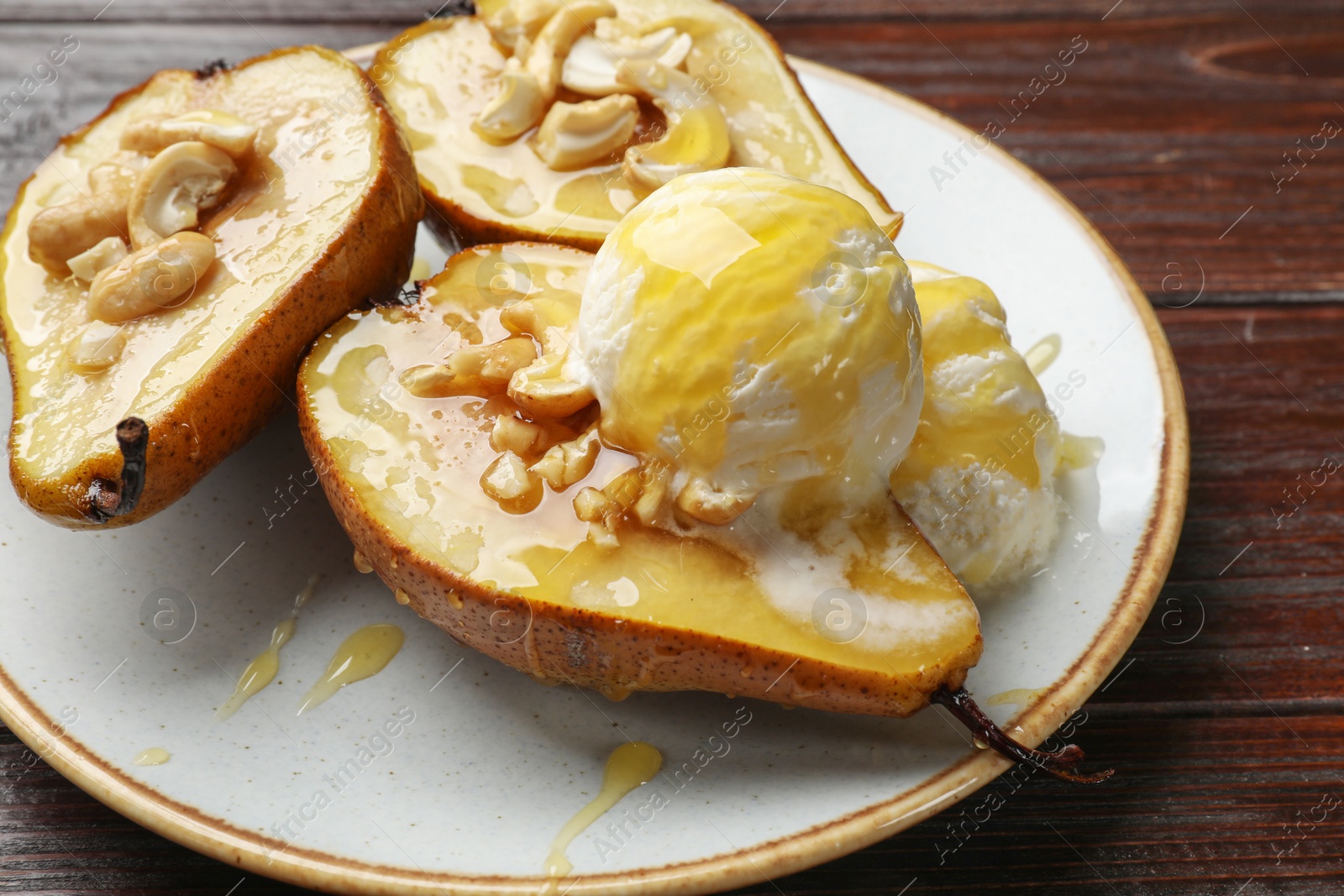 Photo of Delicious baked pears with nuts, ice cream and honey on wooden table, closeup