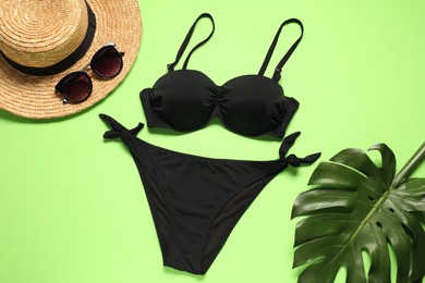 Flat lay composition with black swimsuit, sunglasses and hat on green background