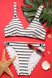 Photo of Striped swimsuit, sunglasses, starfishes and monstera leaf on red background, flat lay