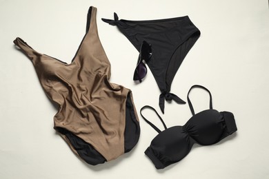 Photo of Beautiful swimsuits and sunglasses on light background, flat lay