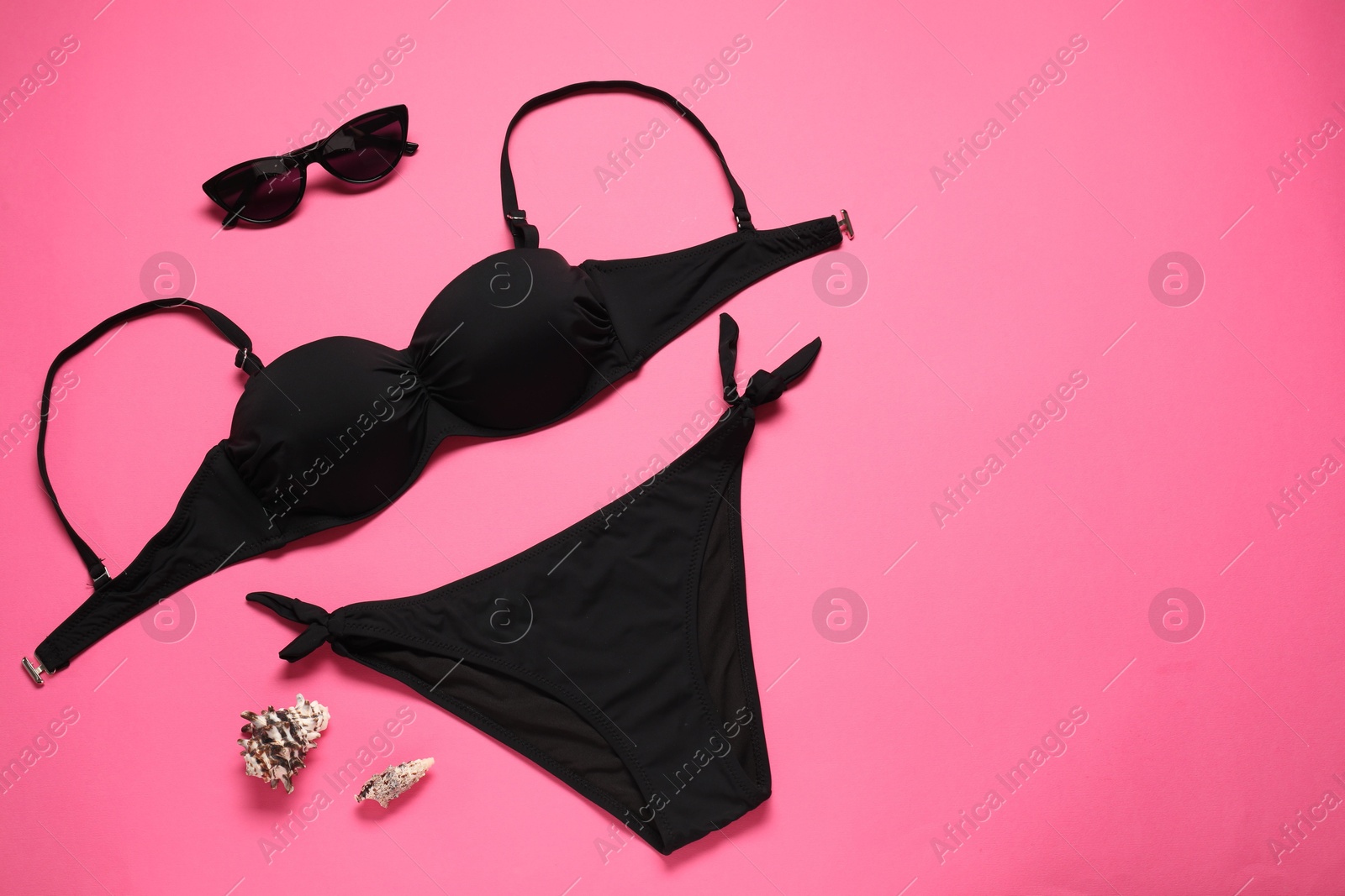 Photo of Black swimsuit, sunglasses and seashells on pink background, flat lay. Space for text