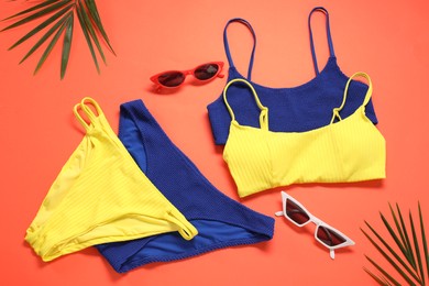 Flat lay composition with beautiful swimsuits and sunglasses on coral background