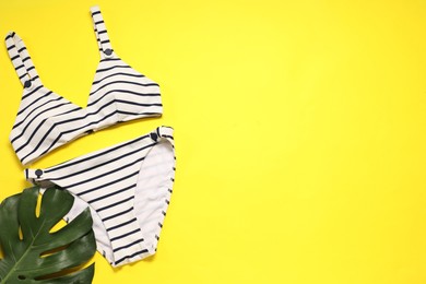 Photo of Striped swimsuit and monstera leaf on yellow background, flat lay. Space for text