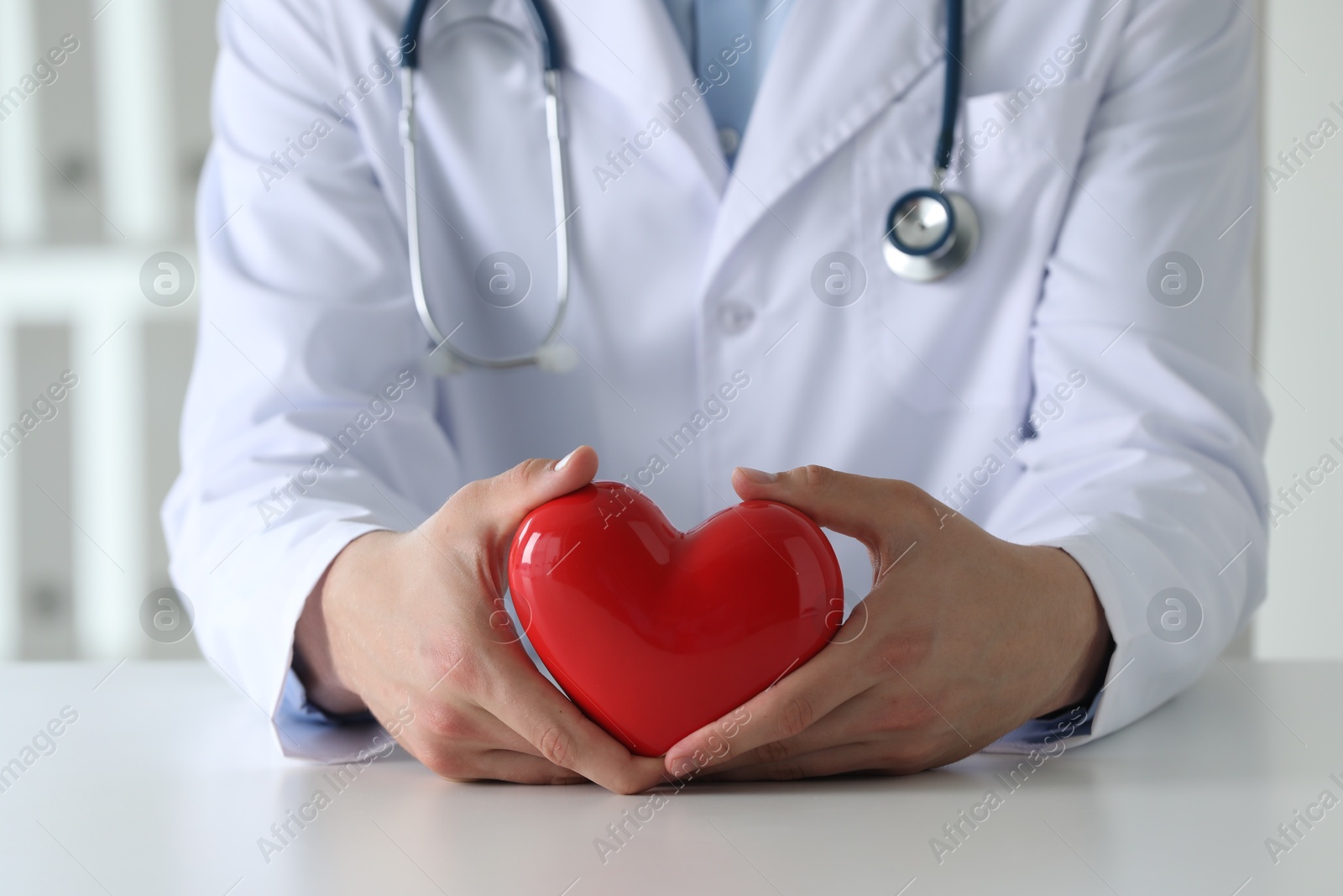 Photo of Doctor with red heart at white table in clinic, closeup