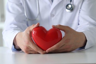 Photo of Doctor with red heart at white table, closeup