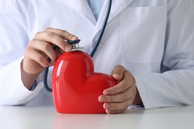 Photo of Doctor with stethoscope and red heart at white table, closeup