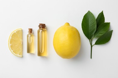 Bottles of essential oils, lemon and green leaves on white background, flat lay