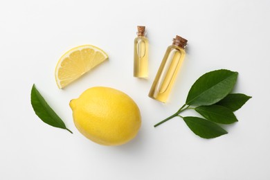 Bottles of essential oils, lemon and green leaves on white background, flat lay