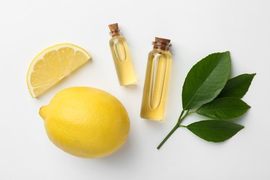 Photo of Bottles of essential oils, lemon and green leaves on white background, flat lay