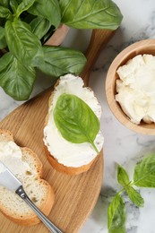 Photo of Pieces of bread with cream cheese and basil served on white marble table, flat lay