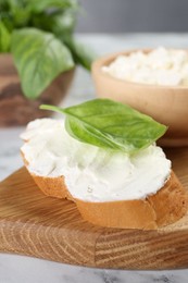 Photo of Piece of bread with cream cheese and basil leaf on white table, closeup