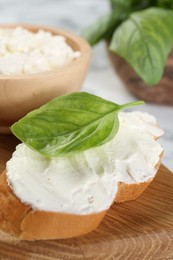 Photo of Piece of bread with cream cheese and basil leaf on white table, closeup