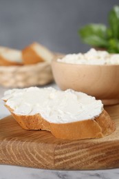 Photo of Piece of bread with cream cheese on white marble table, closeup