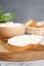 Piece of bread with cream cheese on white marble table, closeup