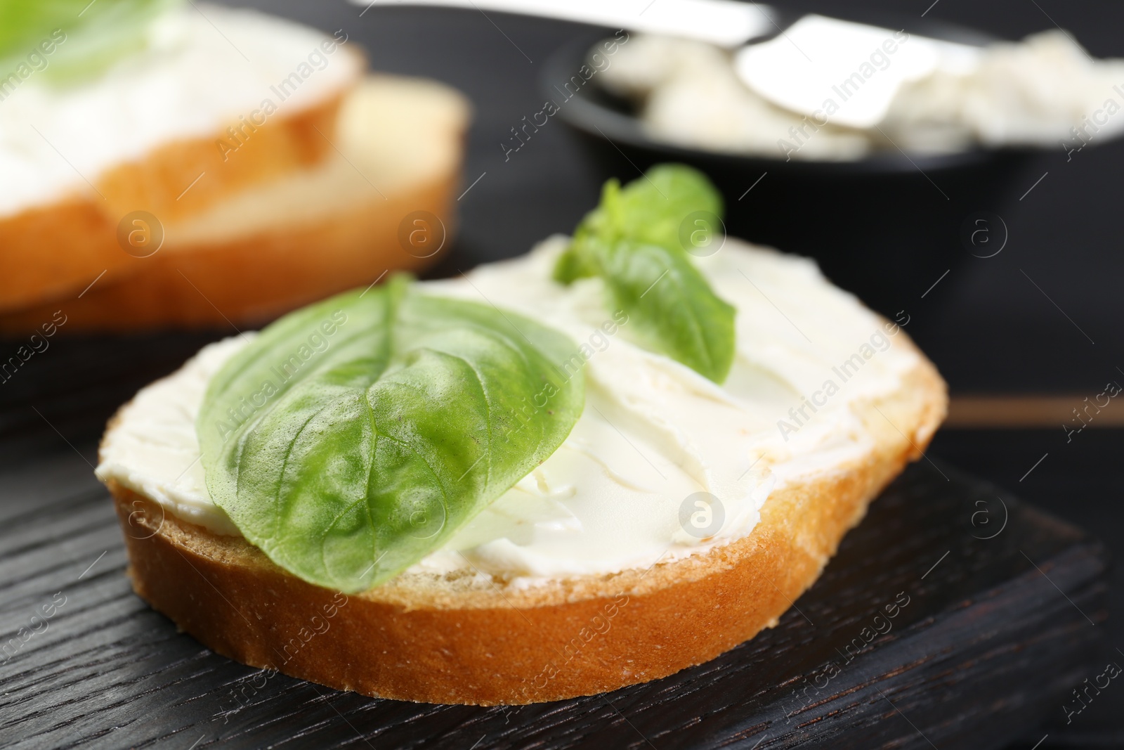 Photo of Piece of bread with cream cheese and basil on black table, closeup