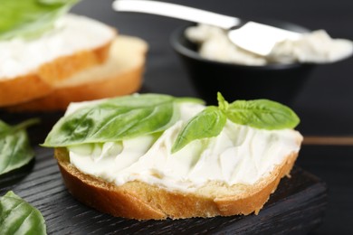 Photo of Piece of bread with cream cheese and basil on black table, closeup