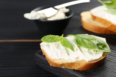 Photo of Piece of bread with cream cheese and basil on black wooden table, closeup. Space for text