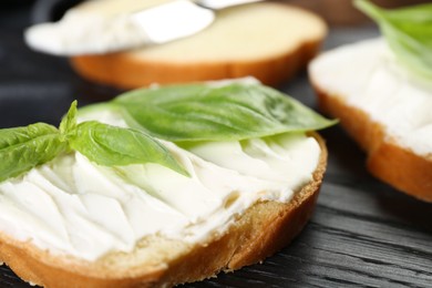 Photo of Piece of bread with cream cheese and basil on black wooden table, closeup