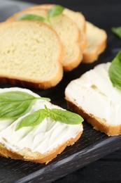 Photo of Pieces of bread with cream cheese and basil leaves on black table, closeup