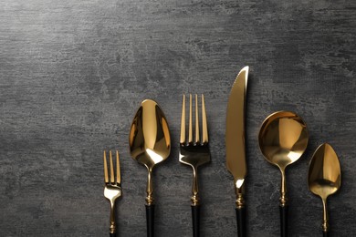 Photo of Elegant golden cutlery set on dark grey table, flat lay. Space for text