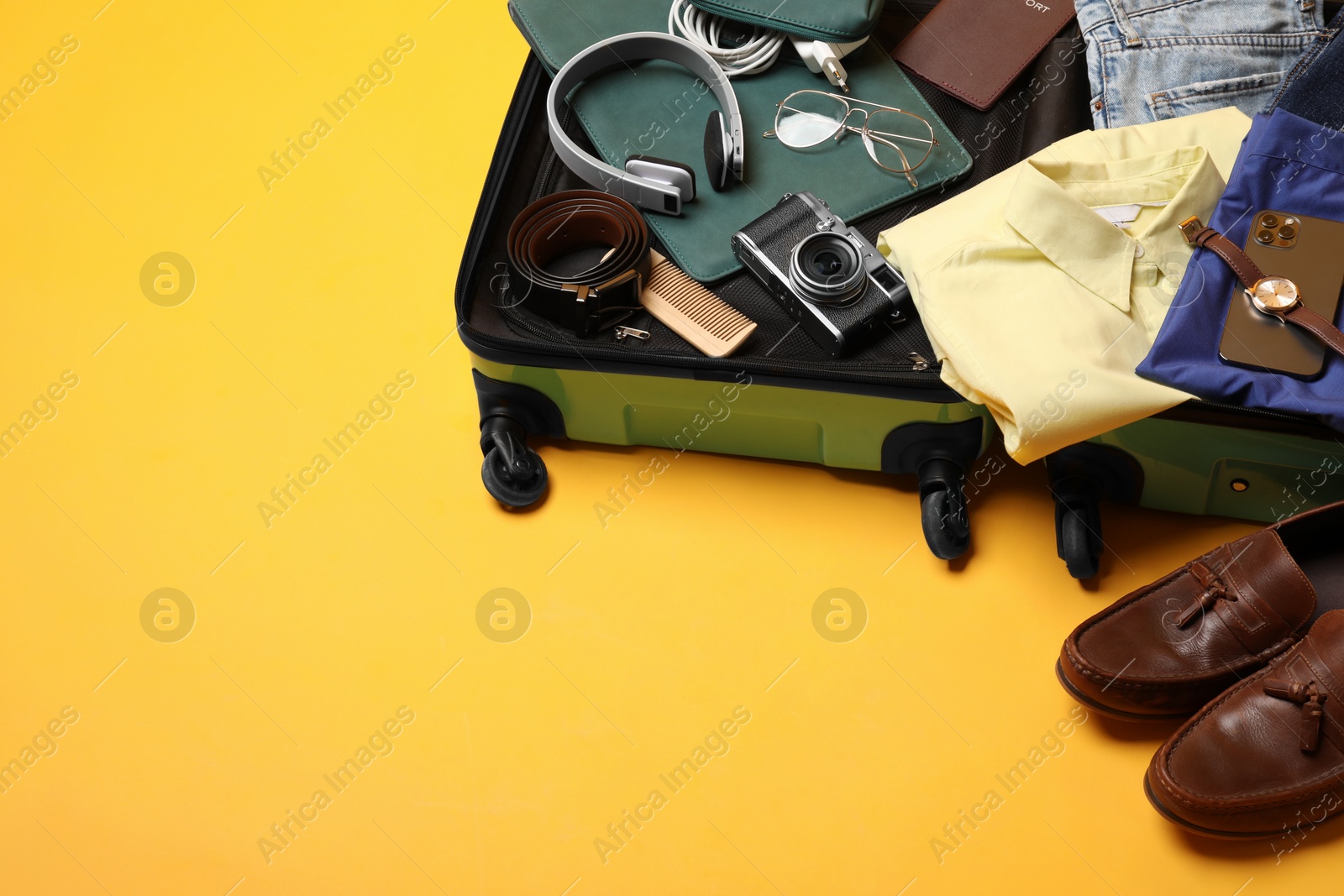 Photo of Open suitcase with traveler's belongings on yellow background, space for text