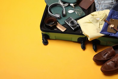 Photo of Open suitcase with traveler's belongings on yellow background, space for text