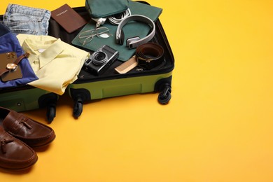 Photo of Open suitcase with traveler's belongings on yellow background, space for text