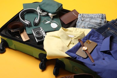 Open suitcase with traveler's belongings on yellow background, closeup