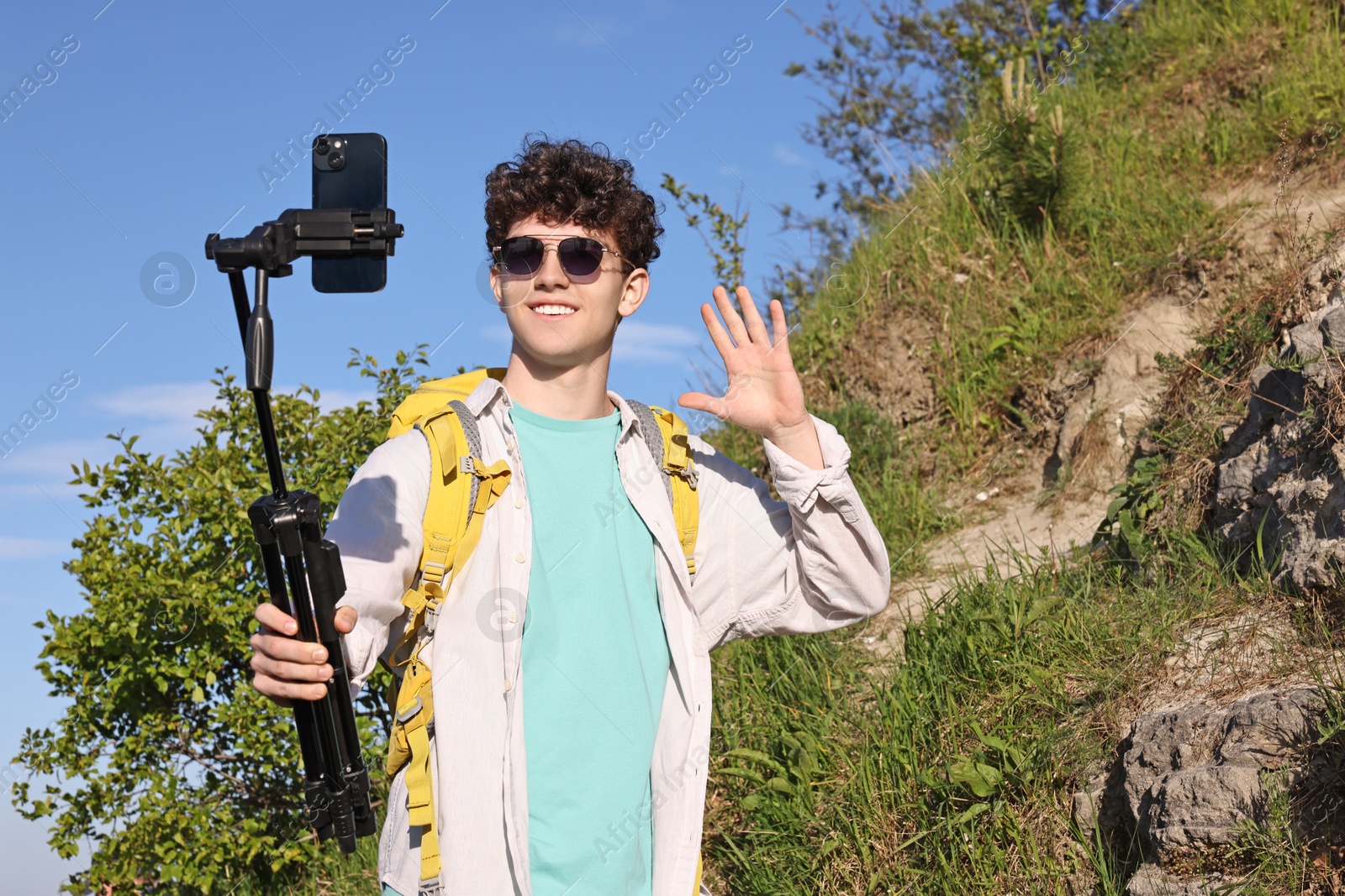 Photo of Travel blogger in sunglasses with smartphone and tripod streaming outdoors