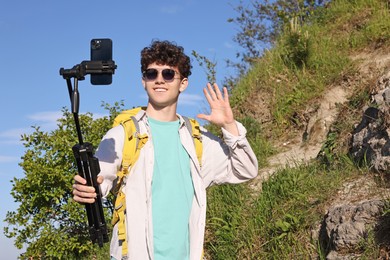 Travel blogger in sunglasses with smartphone and tripod streaming outdoors