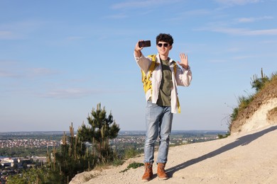 Travel blogger in sunglasses with smartphone streaming outdoors