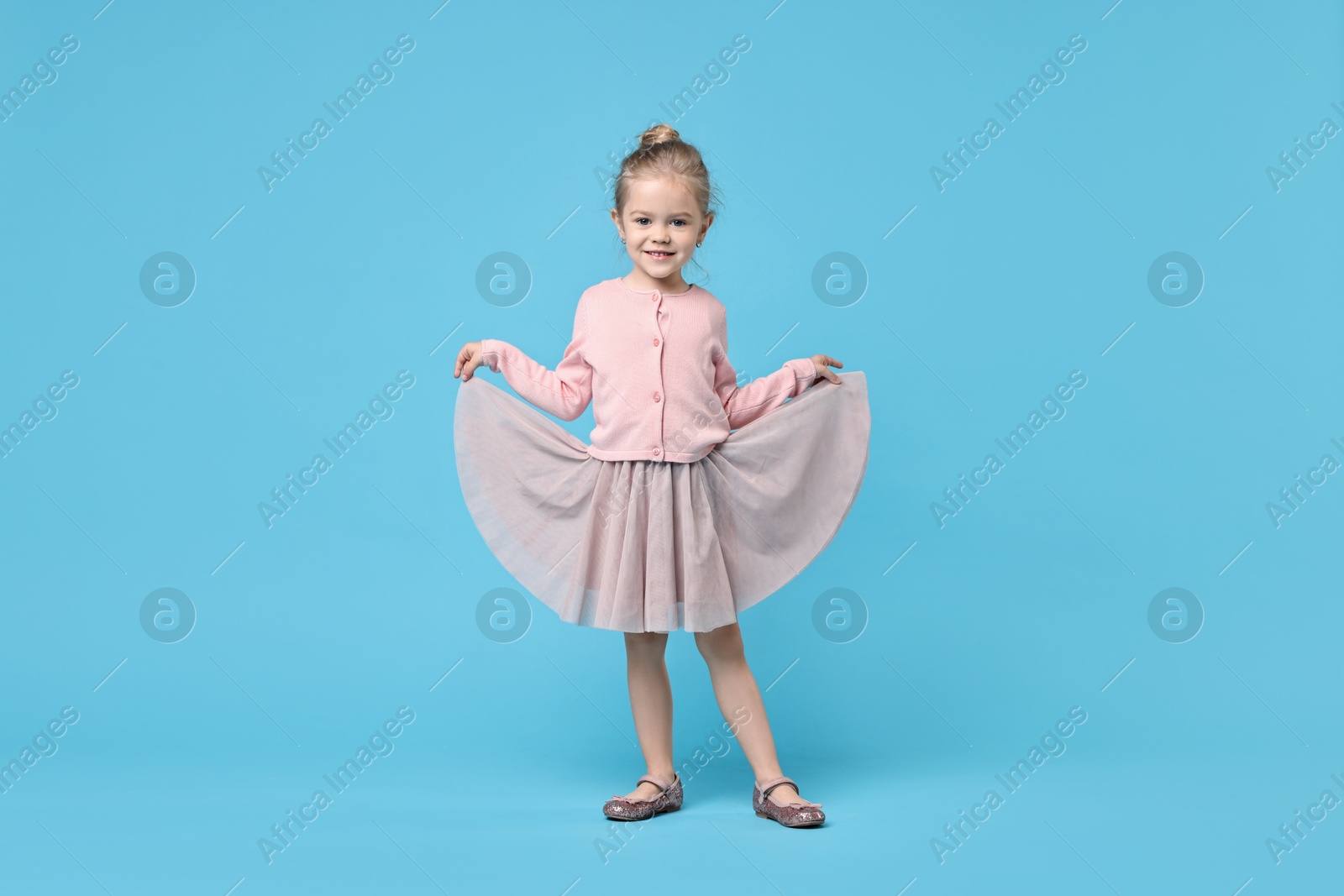 Photo of Cute little girl dancing on light blue background