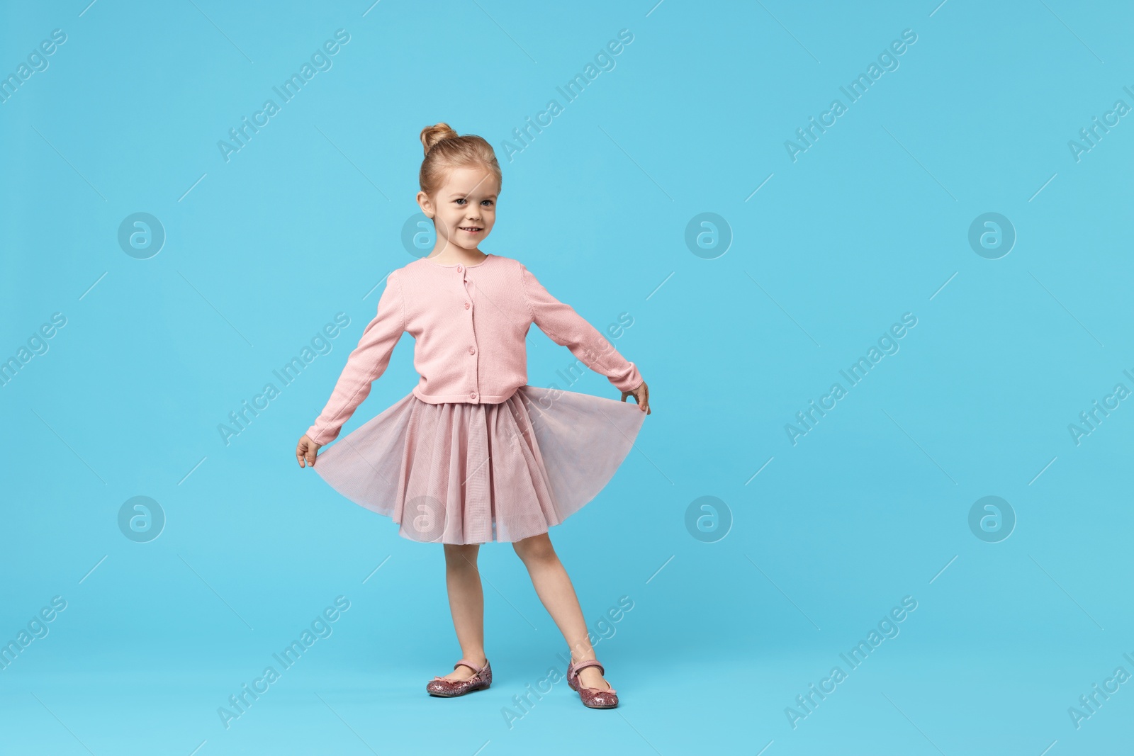 Photo of Cute little girl dancing on light blue background