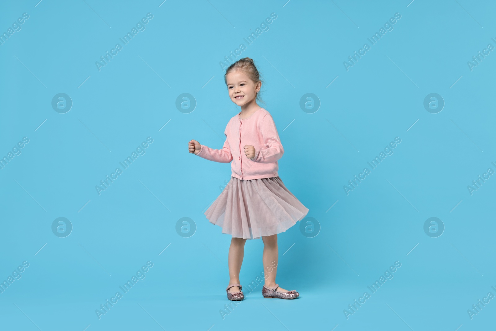 Photo of Cute little girl dancing on light blue background