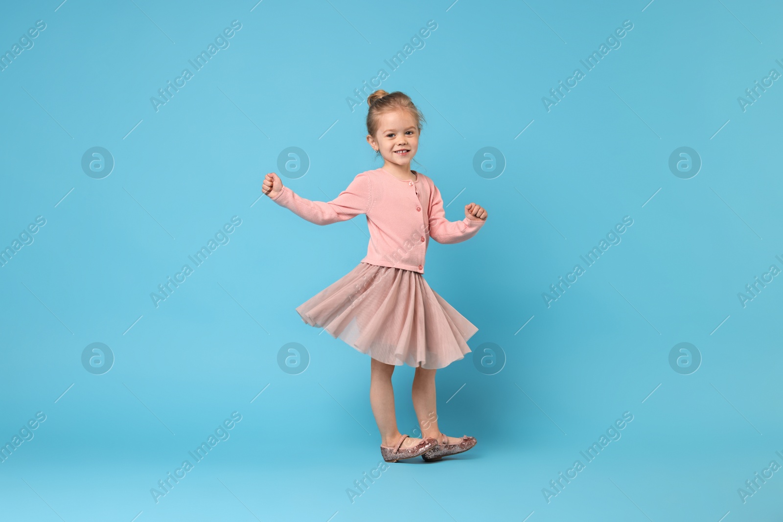 Photo of Cute little girl dancing on light blue background