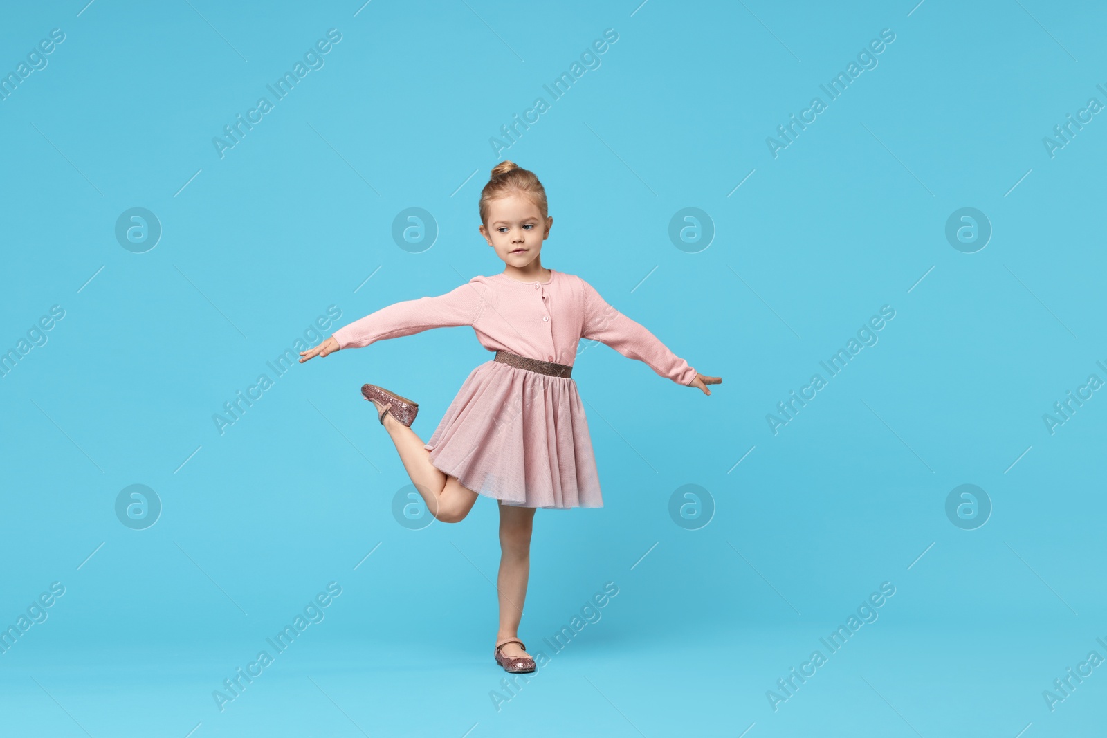 Photo of Cute little girl dancing on light blue background