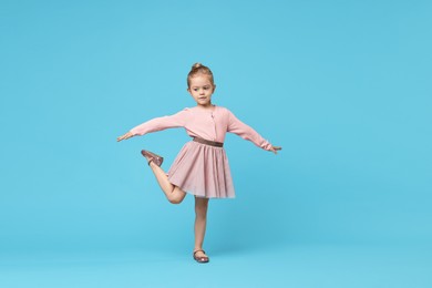 Cute little girl dancing on light blue background