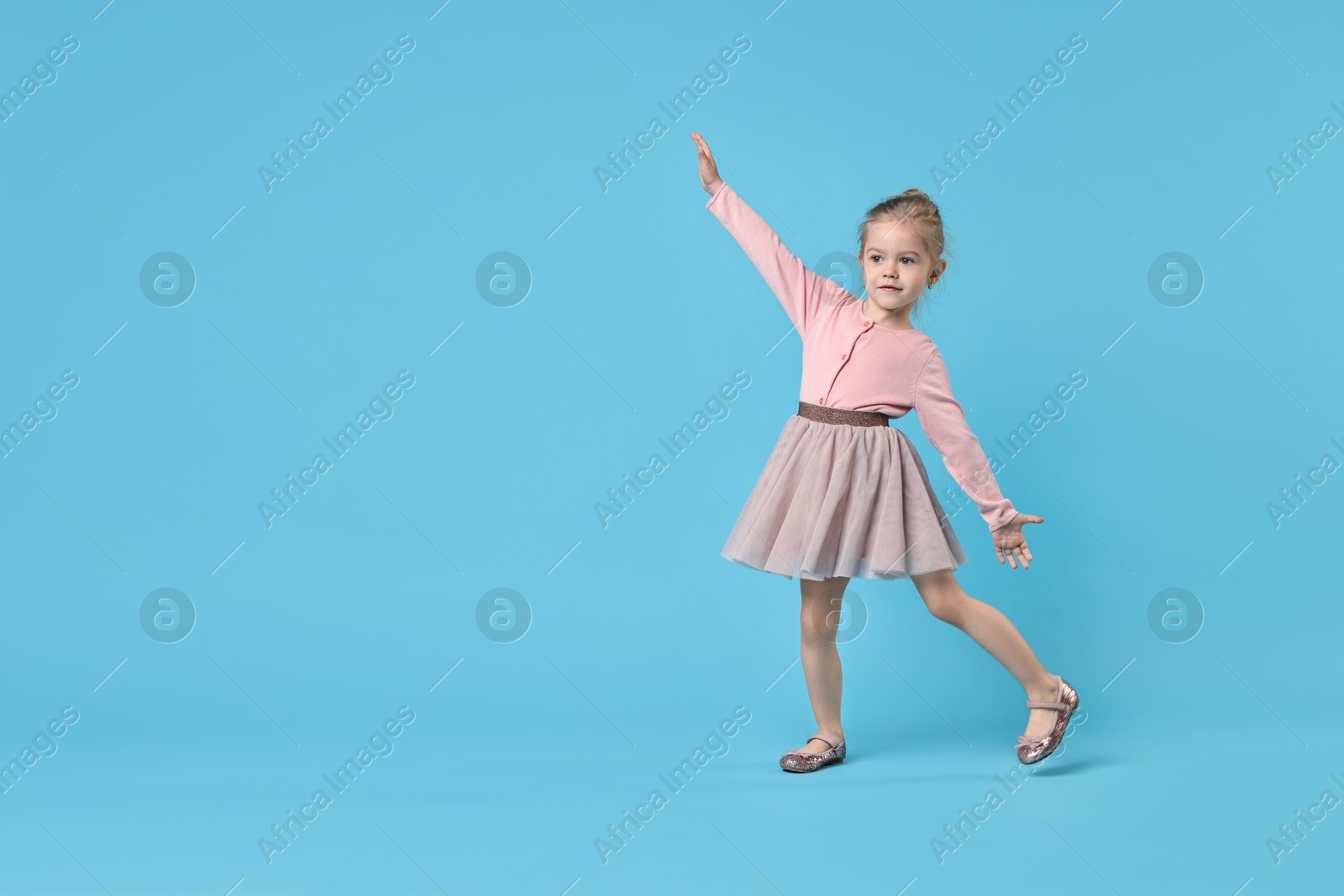 Photo of Cute little girl dancing on light blue background, space for text