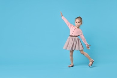 Cute little girl dancing on light blue background, space for text