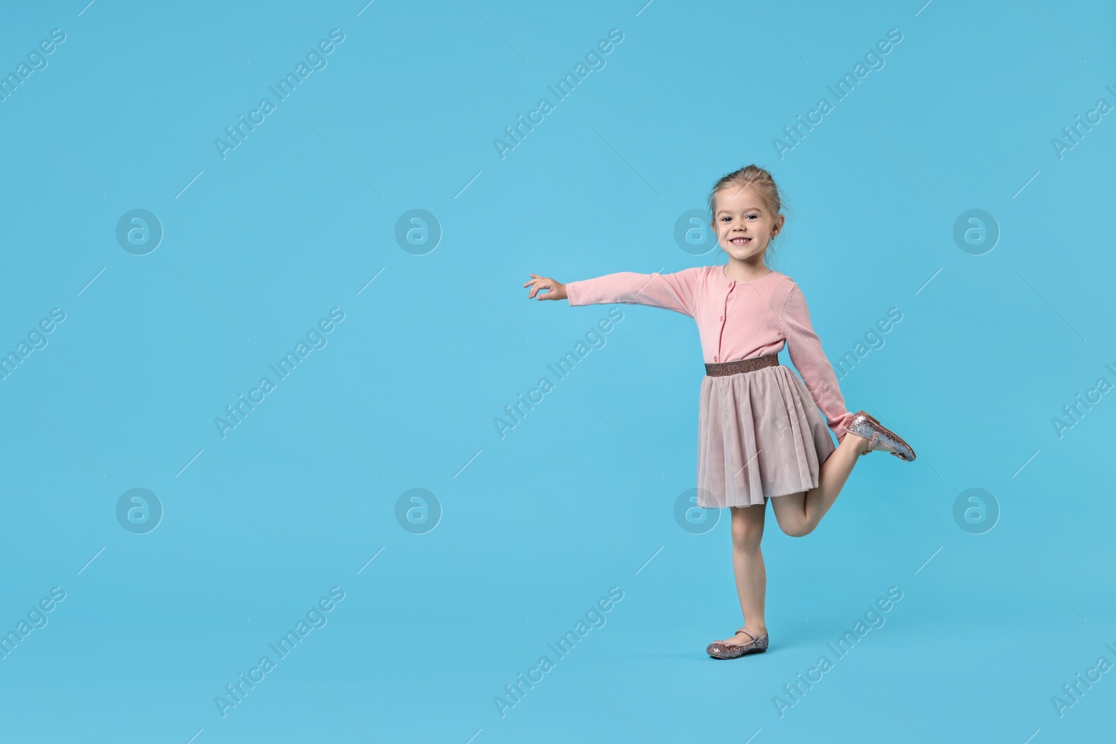 Photo of Cute little girl dancing on light blue background, space for text