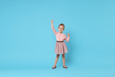 Photo of Cute little girl dancing on light blue background