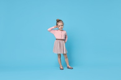 Photo of Cute little girl dancing on light blue background