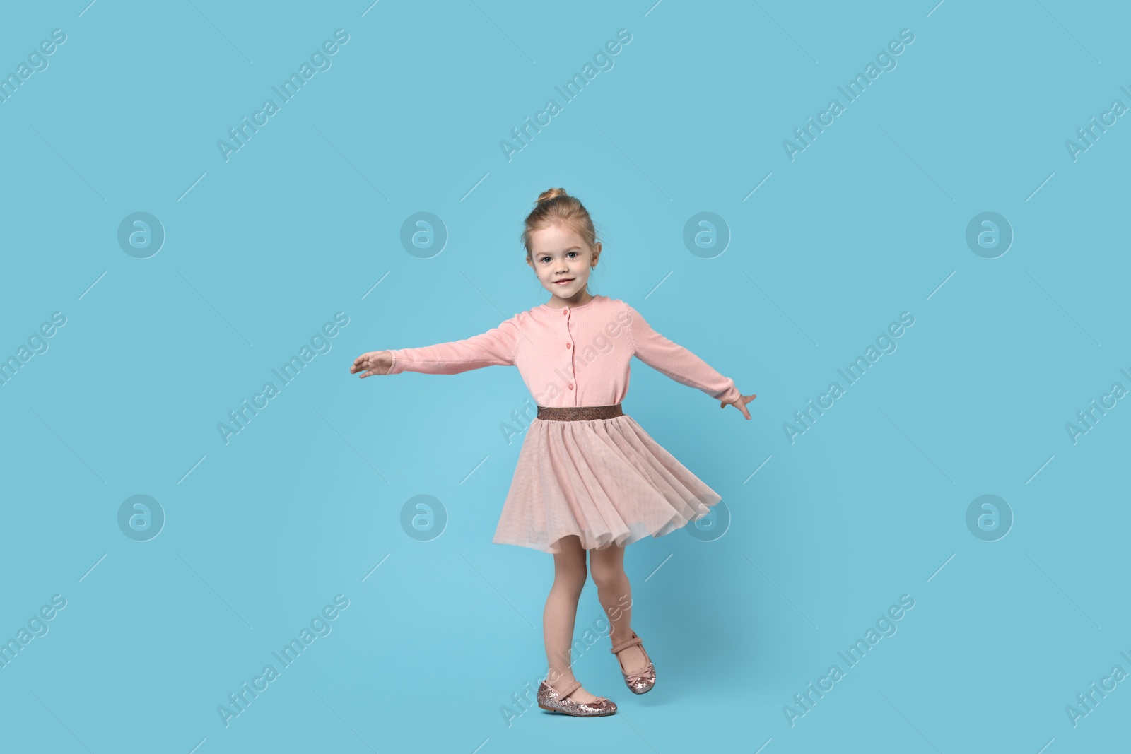 Photo of Cute little girl dancing on light blue background