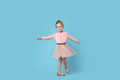 Photo of Cute little girl dancing on light blue background