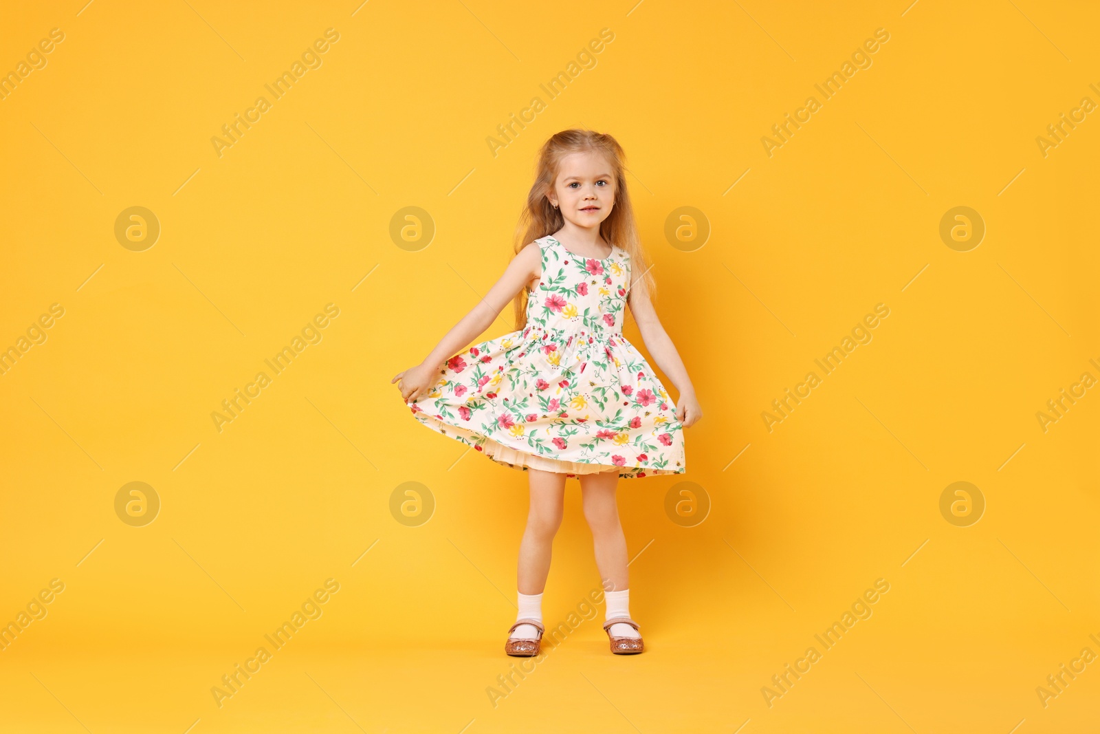 Photo of Cute little girl dancing on orange background