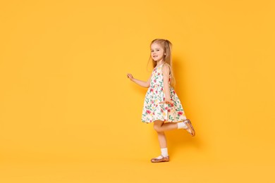 Cute little girl dancing on orange background, space for text