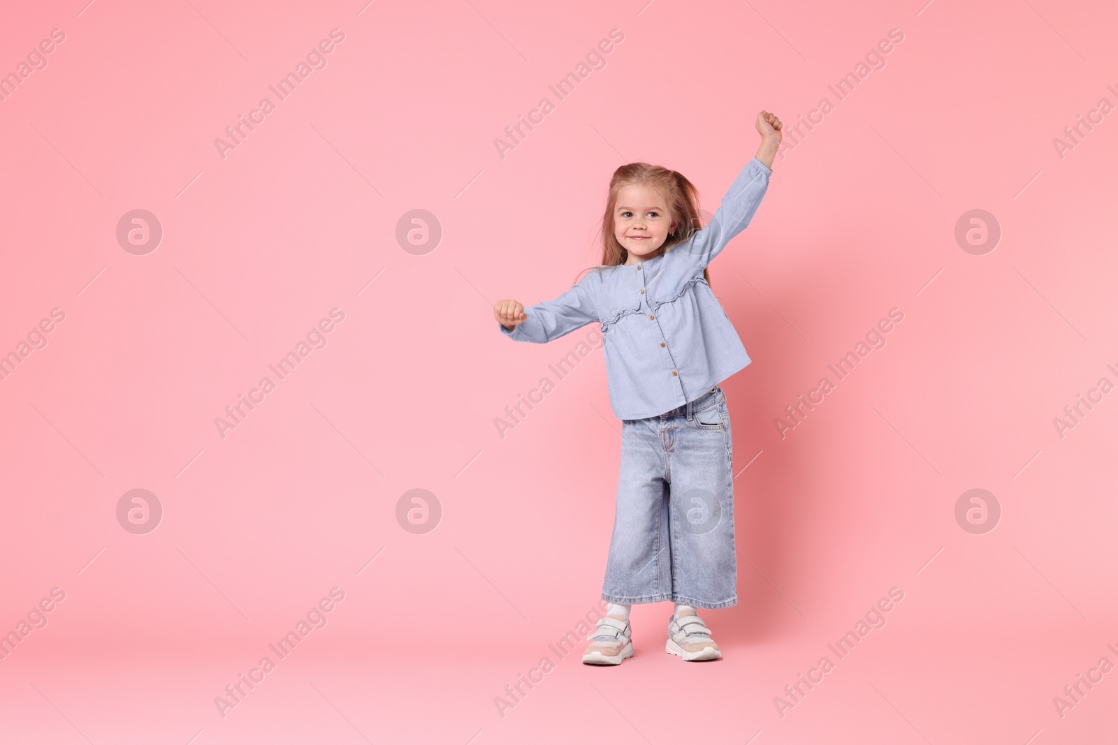 Photo of Cute little girl dancing on pink background, space for text