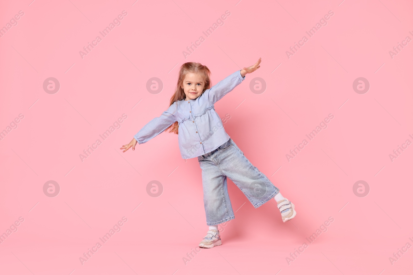 Photo of Cute little girl dancing on pink background